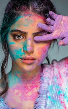 a woman with blue and pink paint on her face holding her hands to her head