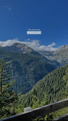 a scenic view of mountains and trees from the top of a wooden fence with a blue sky in the background