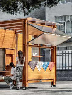 two people standing in front of a wooden structure with an awning on it's side