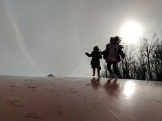 two children are walking on the top of a hill with trees in the background and sun shining through the clouds