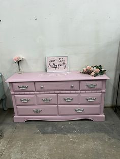 a pink dresser with flowers and a sign on top