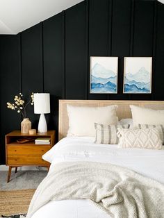 a bedroom with black walls, white bedding and two pictures on the wall above it