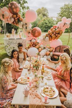 a group of people sitting around a table with food and balloons in the air above them