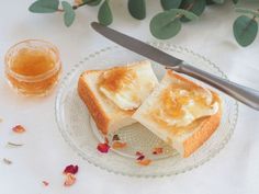 two pieces of bread on a glass plate next to a knife and some tea leaves