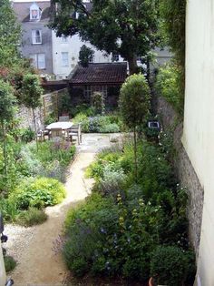 an outdoor garden with lots of plants and flowers on the ground, next to a building