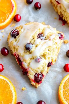 an orange and cranberry scones with icing next to sliced oranges