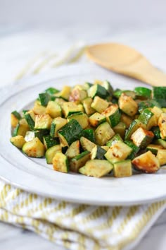 a white plate topped with zucchini on top of a table next to a wooden spoon