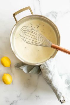 a metal pan filled with liquid next to lemons on a marble counter top and a wooden whisk