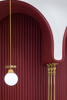 two lamps hanging from the ceiling in front of a red wall with vertical lines on it