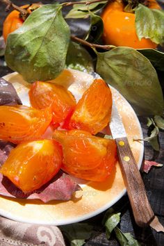 some oranges are sitting on a plate next to leaves and a knife with a wooden handle