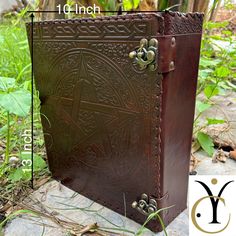 a large brown leather book sitting on top of a stone floor next to grass and plants