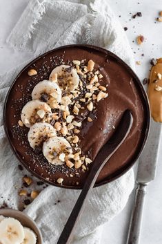 a chocolate dessert with banana slices and nuts on top, next to two bowls of peanut butter