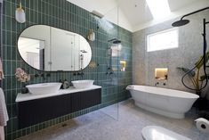 a large bathroom with two sinks and a bathtub in the center, surrounded by green tiles