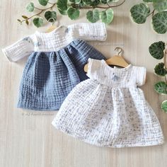 two baby clothes sitting on top of a wooden floor next to green plants and leaves