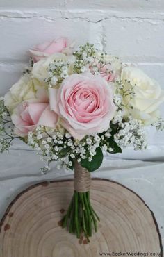 a bouquet of pink and white flowers sitting on top of a wooden slice with baby's breath