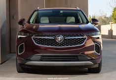 the front end of a maroon buick suv parked in a driveway next to a building