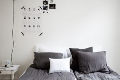 a bed with grey linens and pillows in a white room next to a clock on the wall