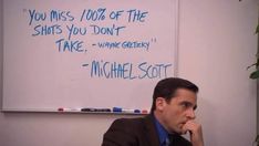 a man sitting at a desk in front of a whiteboard with writing on it