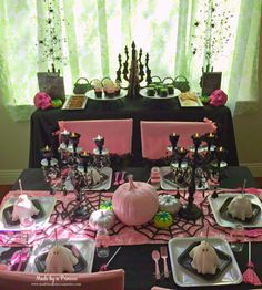 a table set up with pink and black decorations for halloween dinnerware, including pumpkins