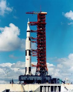 a large rocket sitting on top of a building under a blue sky with white clouds