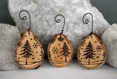 three wooden earrings with trees on them sitting next to some rocks and snowflakes