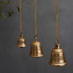 three brass bells hanging from chains on a wall