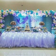 the table is set up for a mermaid themed birthday party with balloons and streamers