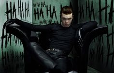 a man sitting in a chair with his hands on his hips and legs crossed, wearing black leather pants