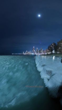 the city skyline is lit up at night as waves crash against the shore and break in the water