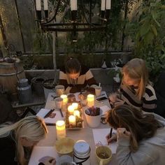 four people sitting at a table with candles on it in front of some books and notebooks