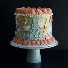 a decorated cake sitting on top of a blue pedestal with flowers and birds painted on it