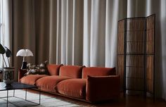 an orange couch sitting in front of a window next to a table with a lamp on it