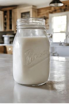 a glass jar filled with white liquid sitting on top of a kitchen counter next to a sink