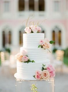 a white wedding cake with pink flowers on top and the word love spelled in gold