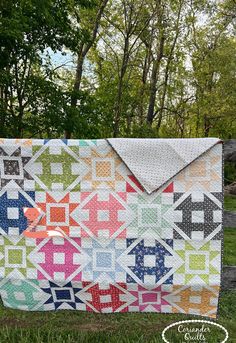 a colorful quilt on the grass with trees in the background and text overlay that says,