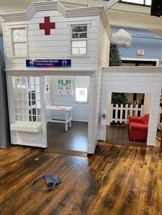 a doll house with a red cross on the roof and white walls, sitting on top of a hard wood floor