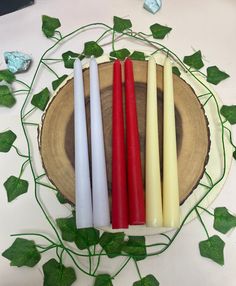 three candles sitting next to each other on top of a wooden plate surrounded by leaves