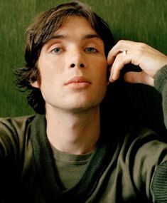 a young man sitting in front of a green wall with his hand on his head