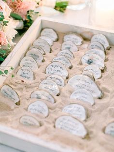 an open box filled with lots of small white heart shaped buttons sitting on top of sand