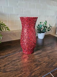 a red vase sitting on top of a wooden table next to a potted plant