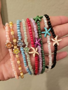 a person is holding several bracelets in their hand, each with different colored beads and starfish charms