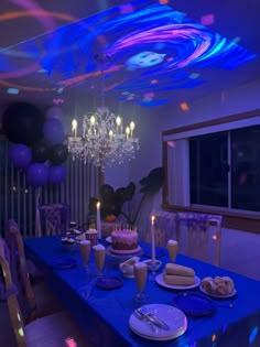 a blue table topped with a cake and lots of candles next to a chandelier