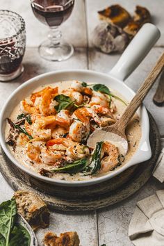 a bowl filled with shrimp and spinach on top of a table next to wine glasses