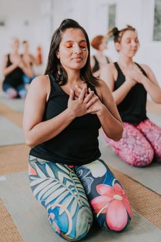 two women sitting on yoga mats with their hands together