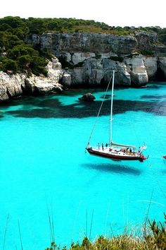 two boats floating in the blue water near cliffs