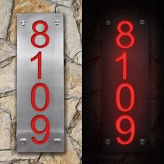 two metal signs with red numbers on them next to a stone wall in the dark