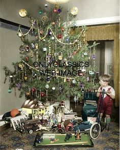 a young boy standing next to a christmas tree in front of a pile of toys