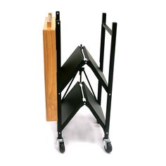 a black metal shelf with two wooden shelves on wheels and one is leaning up against the wall