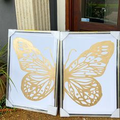 two white and gold butterfly paintings sitting on the side of a building next to a door