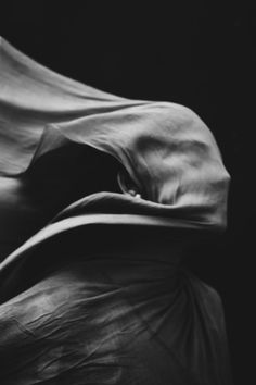 black and white photograph of an unmade bed with sheets pulled over the head on it